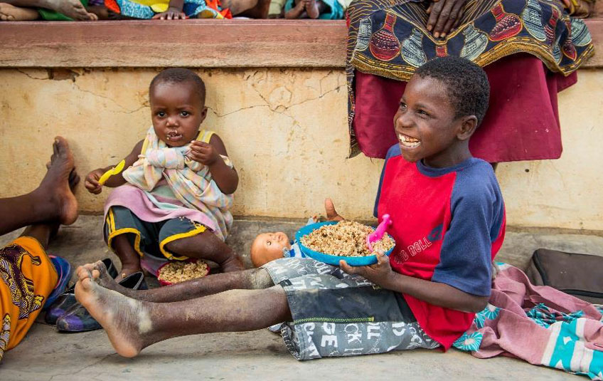 A Malawian boy sitting on the ground eating a bowl of FMSC food.