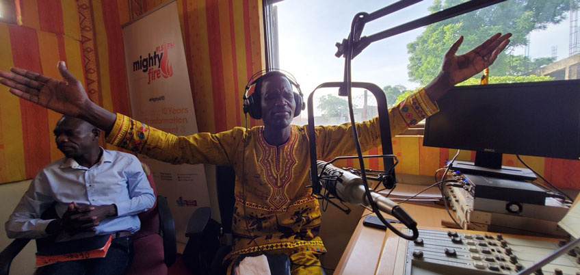 A Ugandan man lifts hands in prayer in a radio studio
