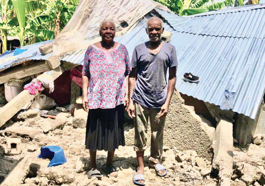an elderly Haitian couple standing in front of a collapsed building