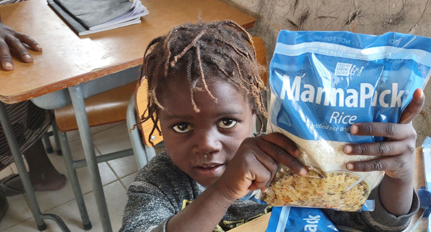 A child in Angola holds up a bag of FMSC food