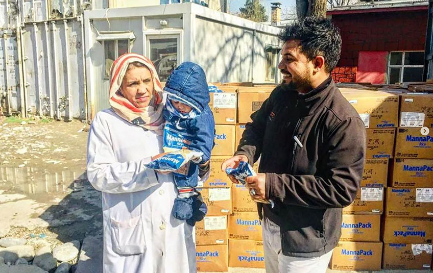 an Afghan woman holds a baby and a pouch of FMSC food