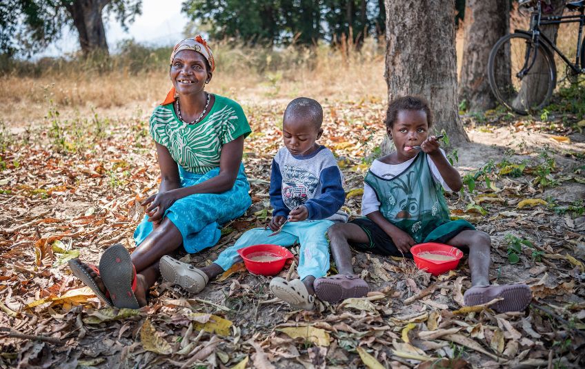 Woman smiling with two children eating from bowls