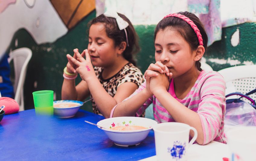Two young girls praying before eating. 