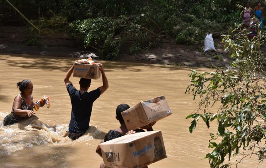 People carrying MannaPack boxes through waist-high water. 