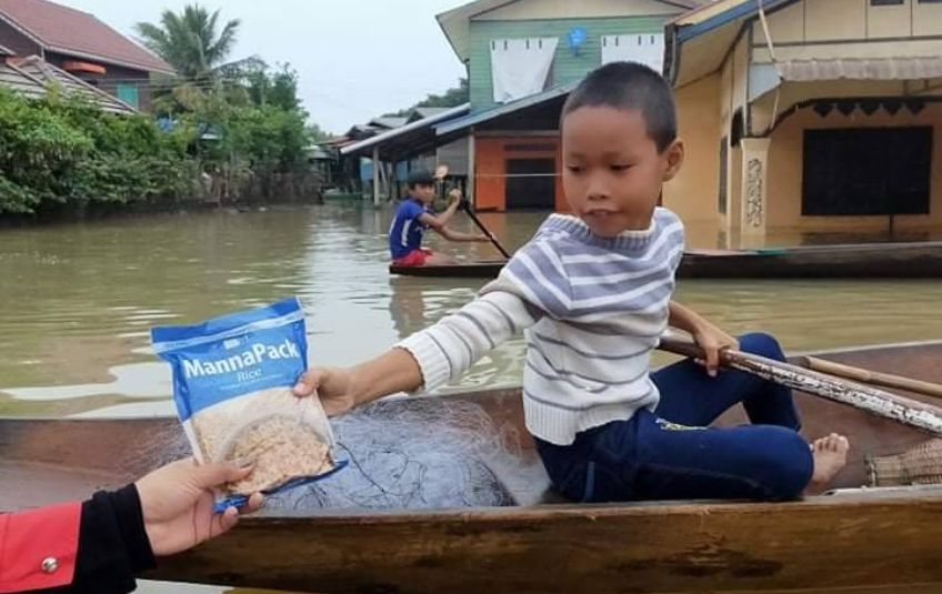 FMSC partner handing MannaPack meal to a boy by boat. 