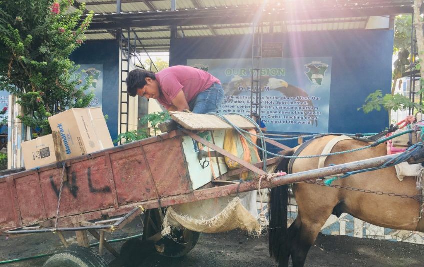 Man loading MannaPack boxes into a wagon being pulled by a horse. 