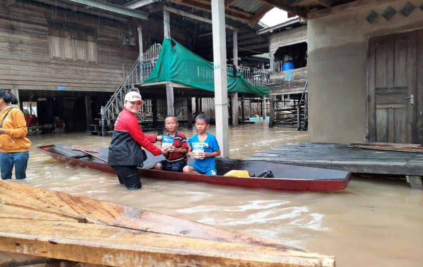 Woman handing MannaPack bags to children in boat. 