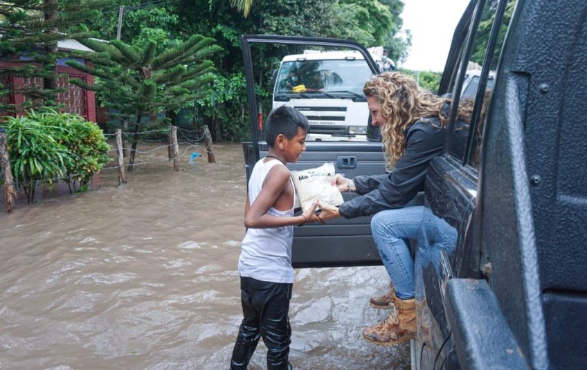 Woman handing FMSC food to boy in flood waters. 
