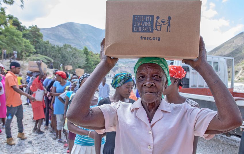 Haitian woman smiling with box of FMSC food on her head