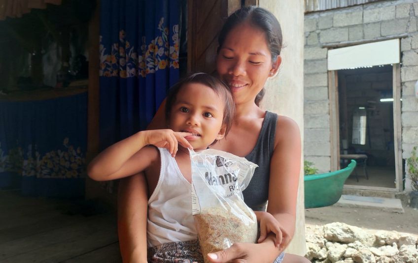 young girl in mother's lap with bag of rice