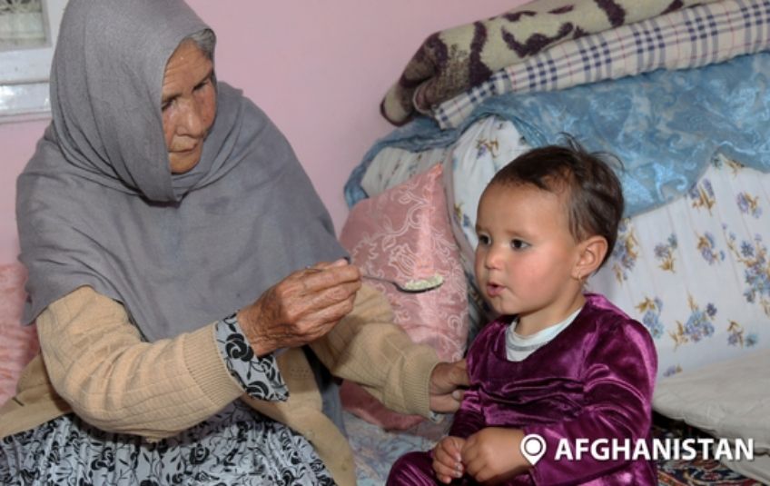 woman with headscarf feeding young girl spoon of rice