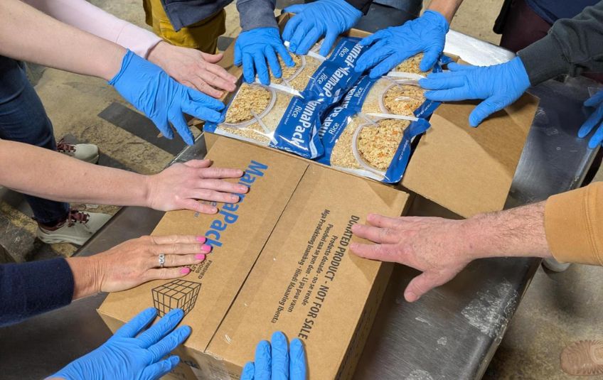 hands in gloves touching box of FMSC food to pray over it