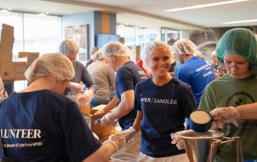 woman in hairnet smiling as she watches people put ingredients in a funnel