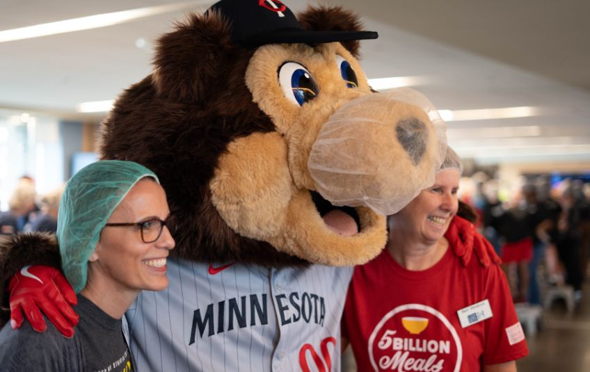 2 women in hairnets pose with Minnesota Twins mascot wearing a beard net