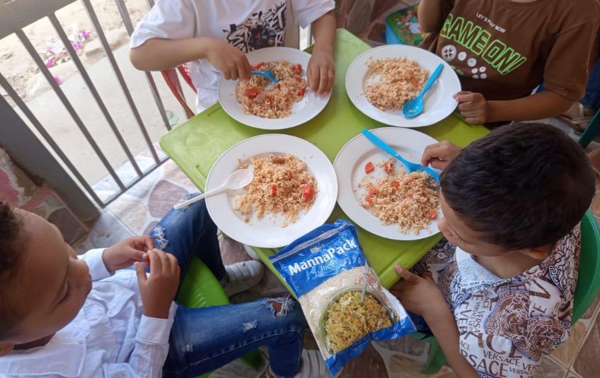 South American children at a table eating food from Christian nonprofit organization Feed My Starving Children