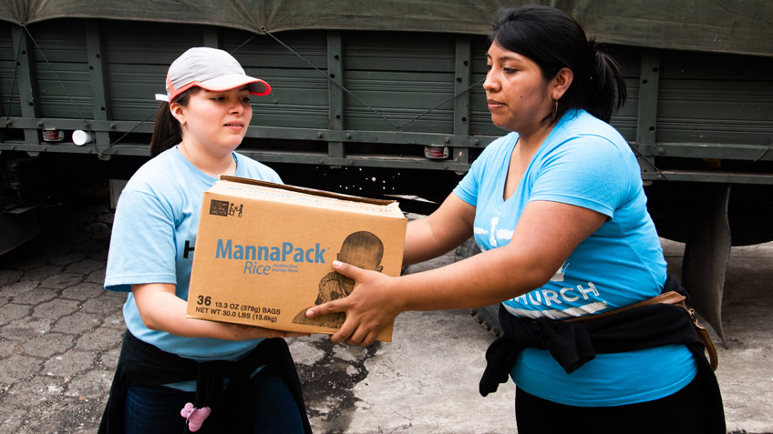 A woman passes a box of FMSC food to another woman