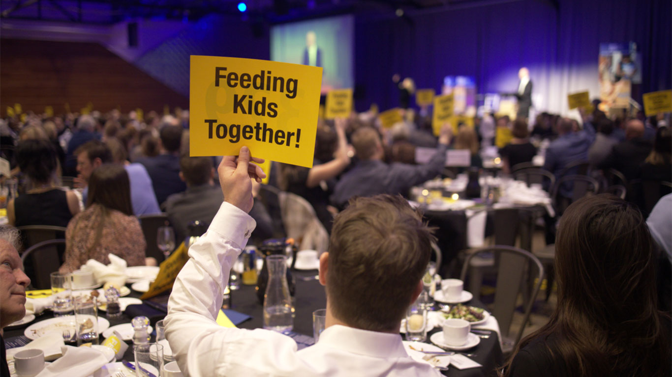 guest holding "Feeding Kids Together" sign at an FMSC gala