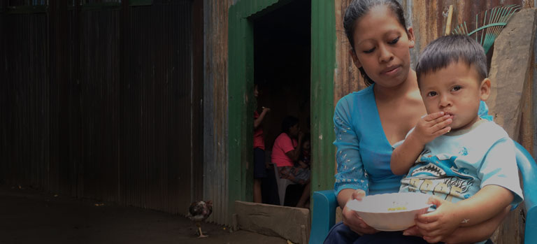 A mother holds a young child eating FMSC food