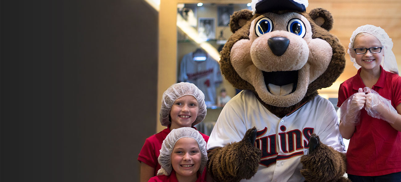 MN Twins mascot TC Bear and three happy kids giving a thumbs-up at Feed My Starving Children's Pack at the Park event