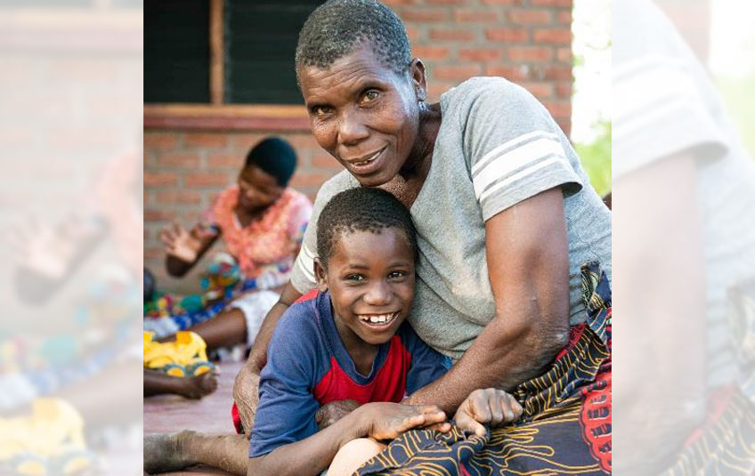 A Malawian boy sitting on his grandmother's lap, both smiling